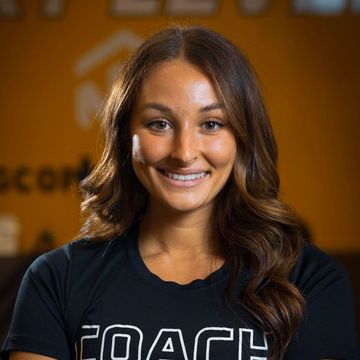 A woman wearing a black coach shirt is smiling for the camera. Coach Taylor