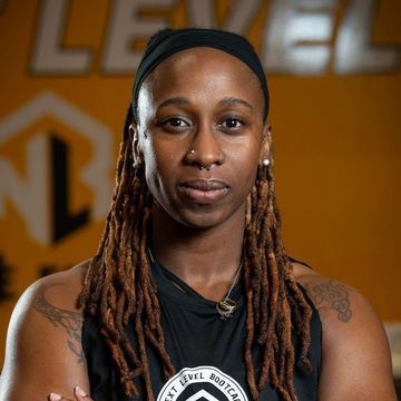 A woman with dreadlocks is wearing a black tank top and a headband. Coach Shawna