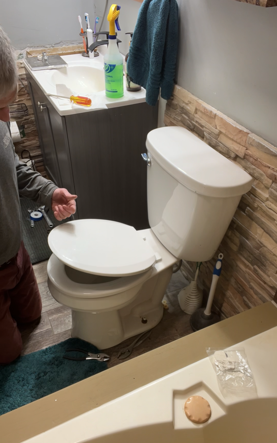 A person is fixing a toilet with a wrench.