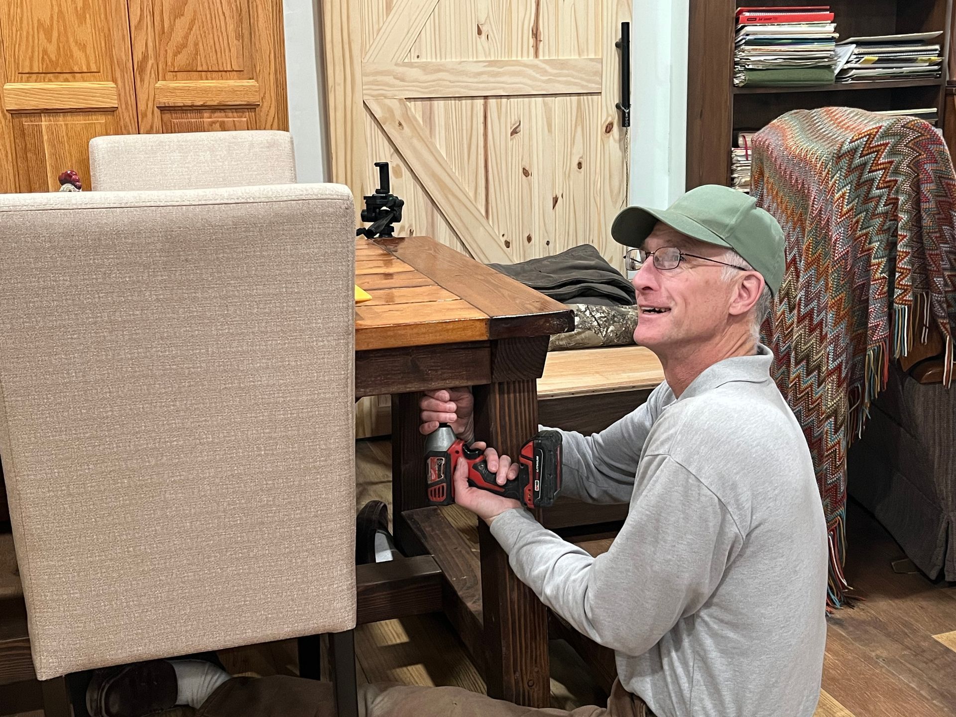 A man is kneeling down next to a wooden table.