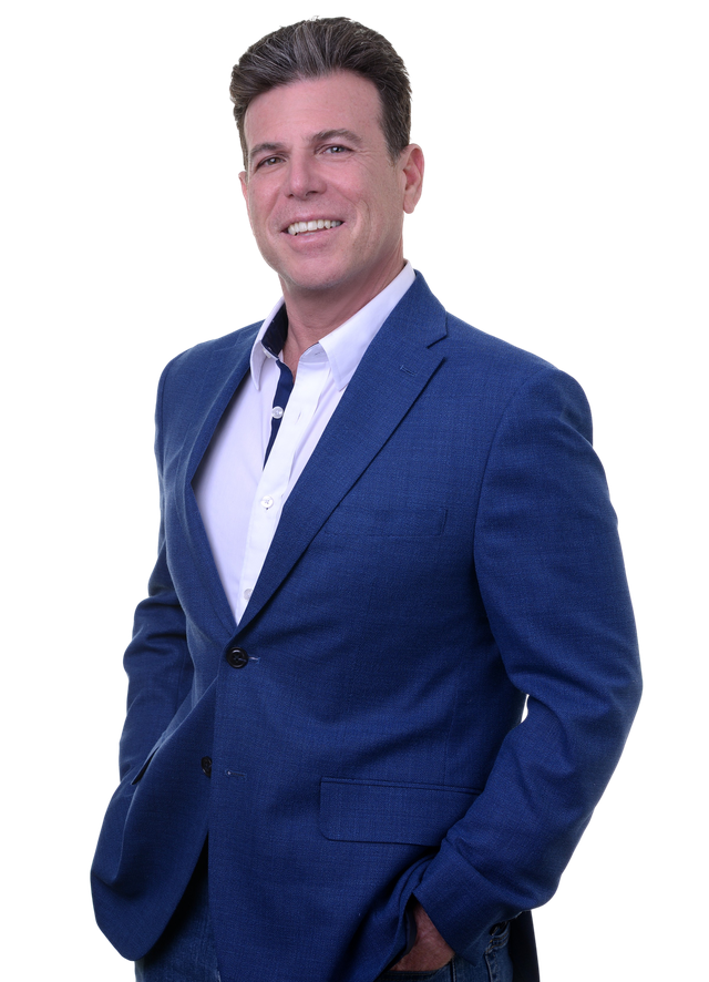 A man in a blue suit and white shirt is smiling with his arms crossed.