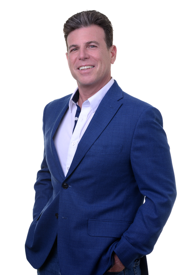 A man in a blue suit and white shirt is smiling with his arms crossed.