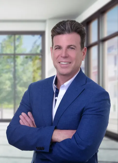 A man in a blue suit and white shirt is smiling with his arms crossed.