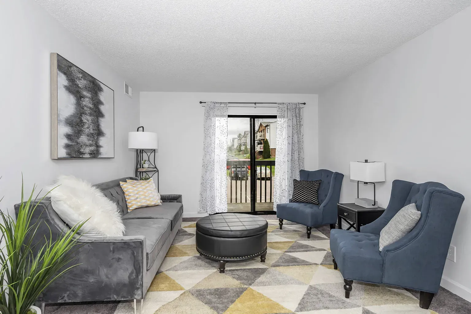 Tall Timber Apartments living room in an apartment with a grey sofa, blue chairs, and a balcony door.