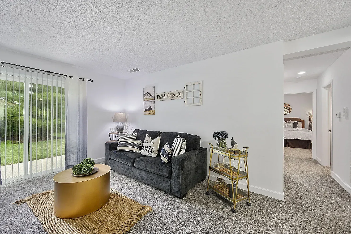 Tall Timber Apartments Living room with a dark gray sofa, gold oval coffee table, rug, and sliding glass doors.