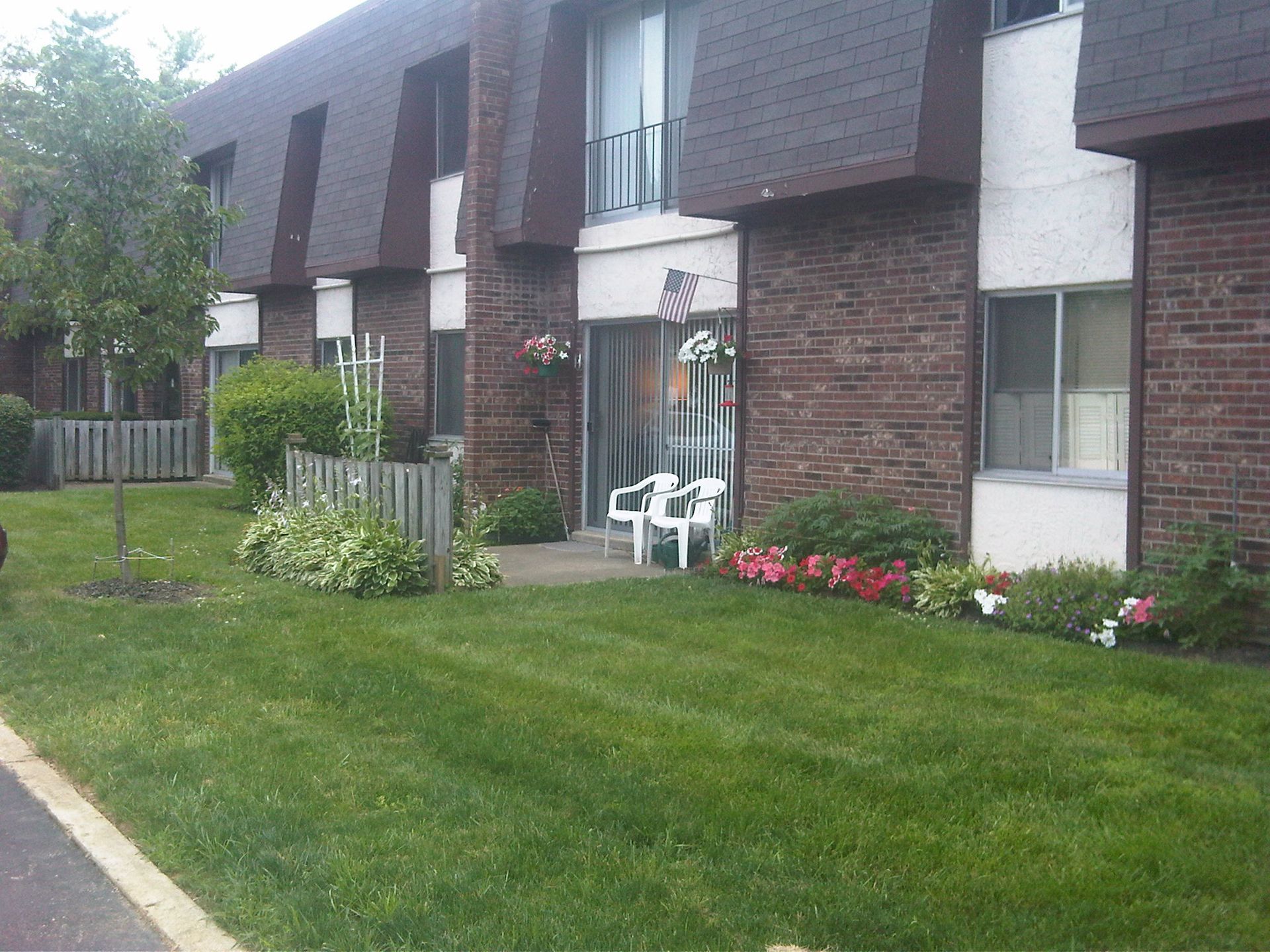 Tall Timber Apartments Front lawn with flower beds and white chairs at brick apartment building entrance.