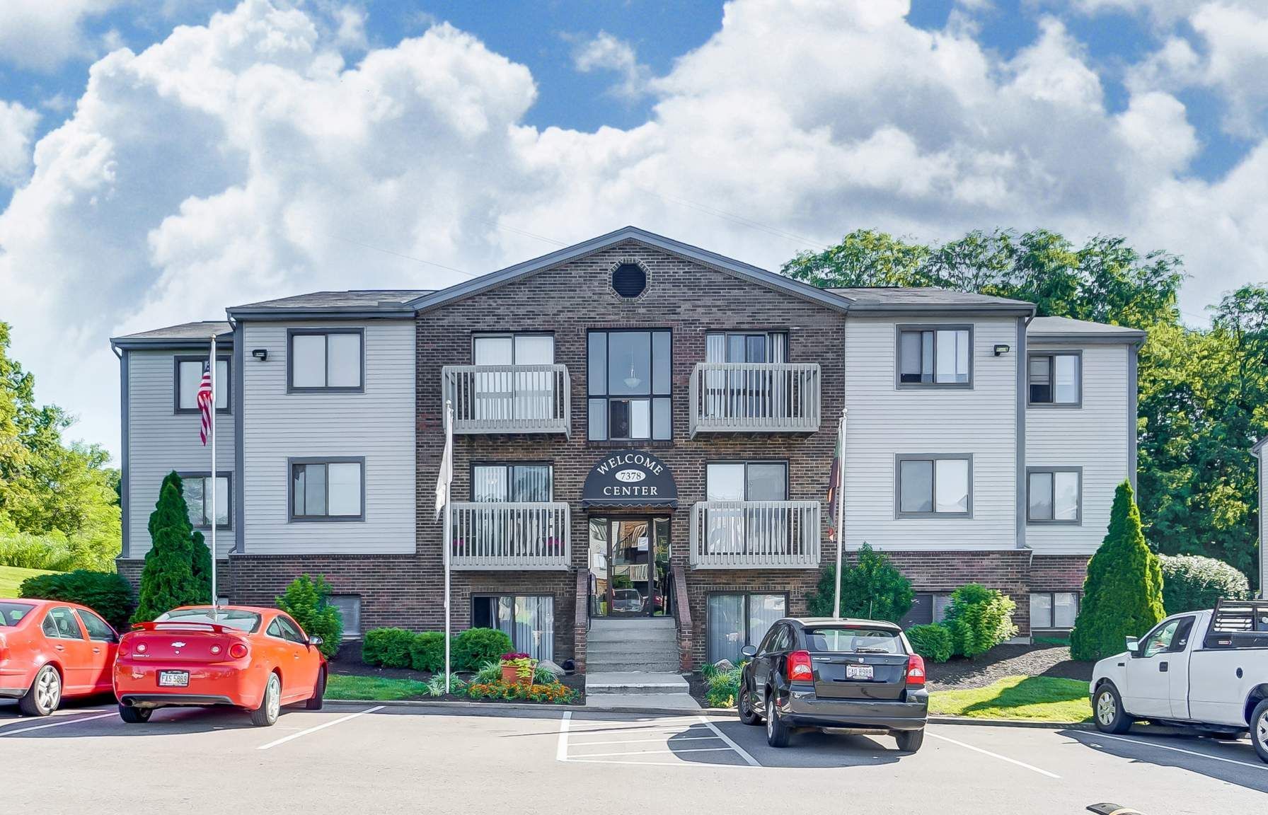 Tall Timber Apartments Exterior view of a three-story multifamily building with brick center and balconies, parking in front.