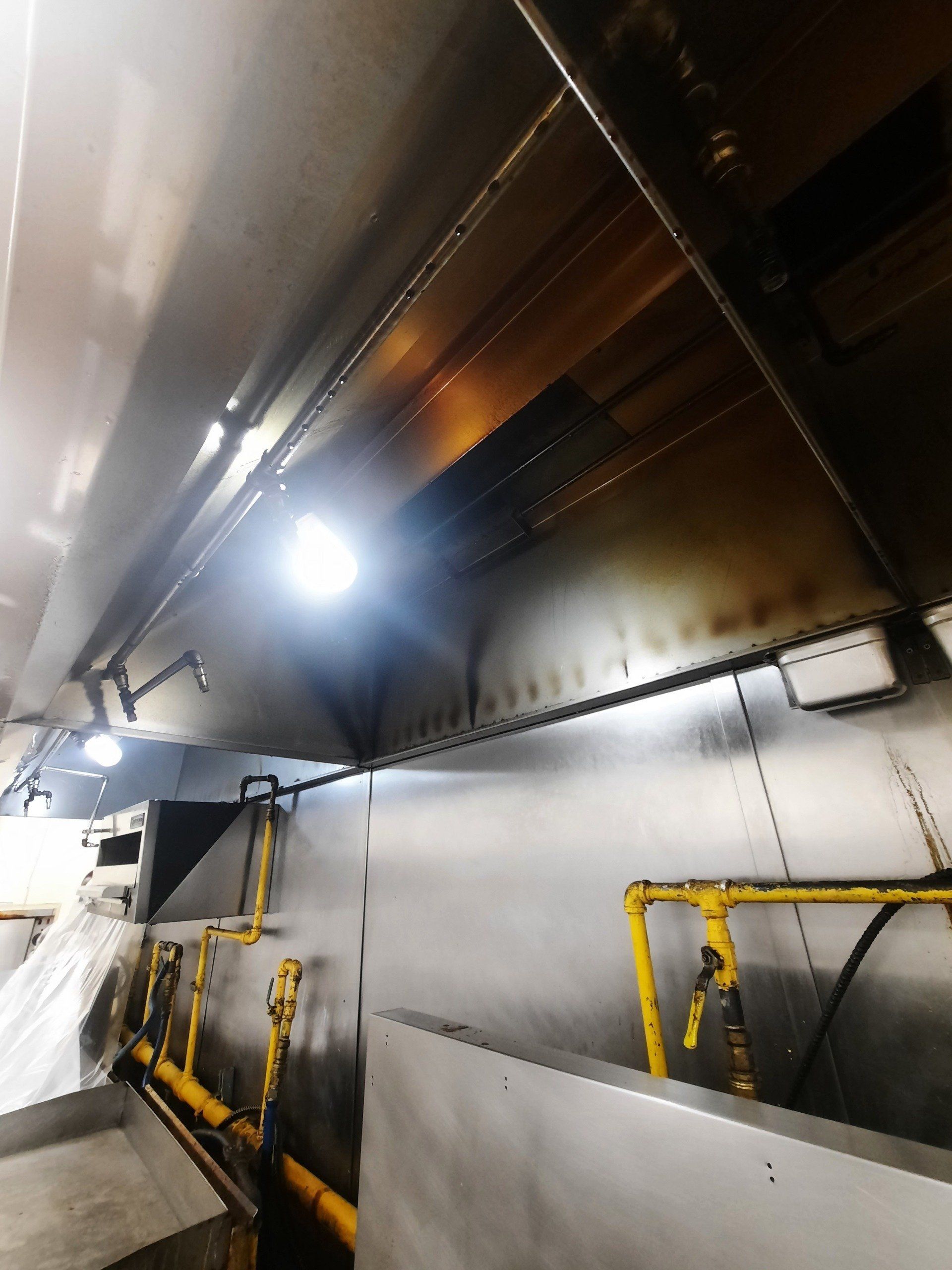 Une cuisine avec une hotte en inox et des tuyaux jaunes