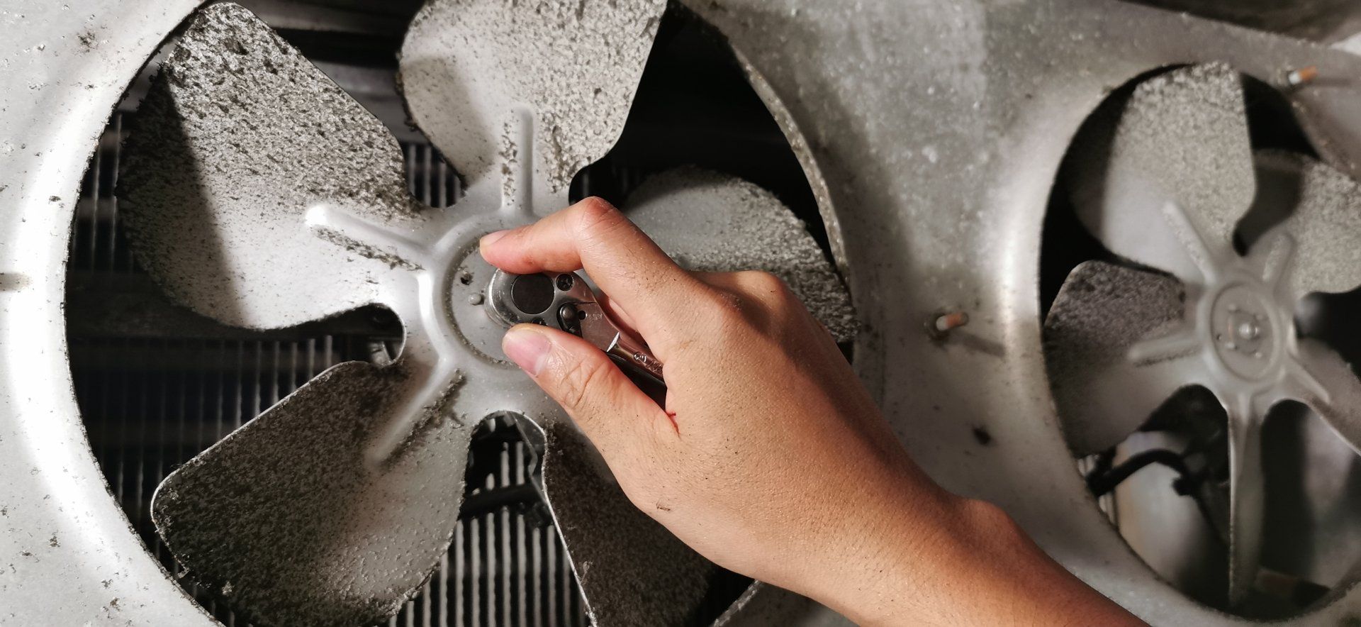 Une personne nettoie un ventilateur sale avec une brosse.