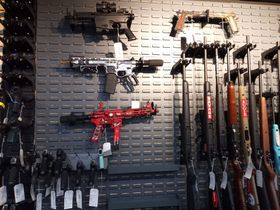 A display wall featuring various rifles and handguns mounted on a pegboard in a store.