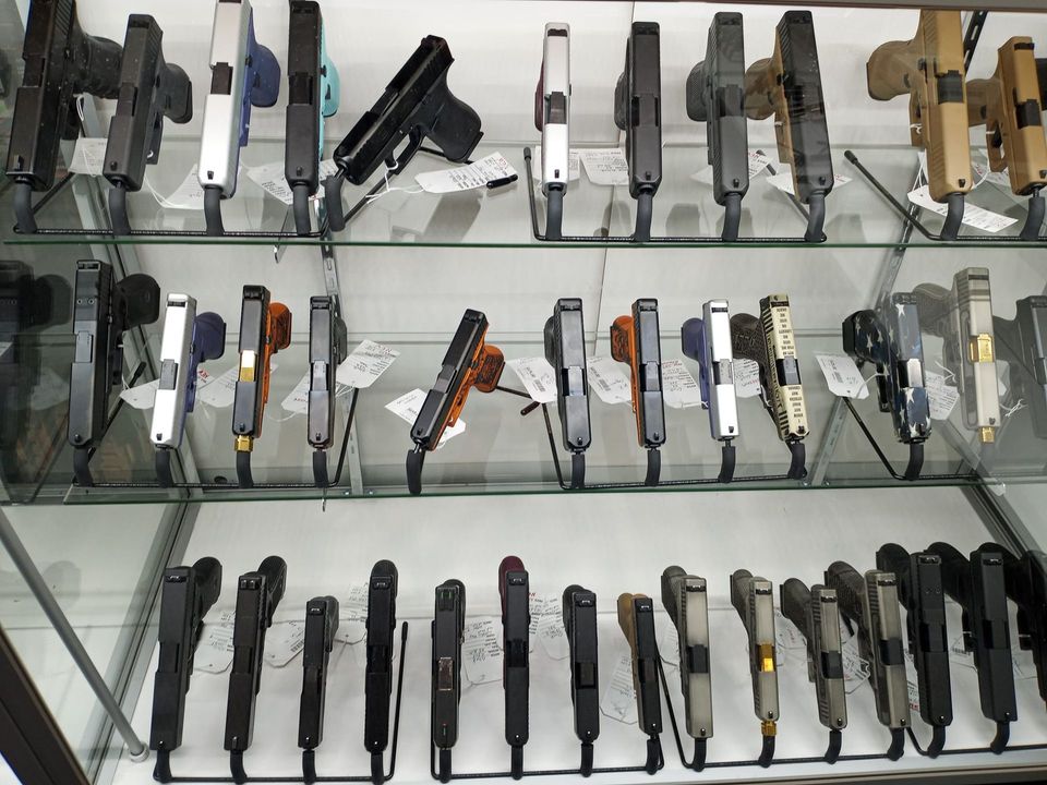 A retail display case containing numerous handguns arranged in rows on glass shelves.