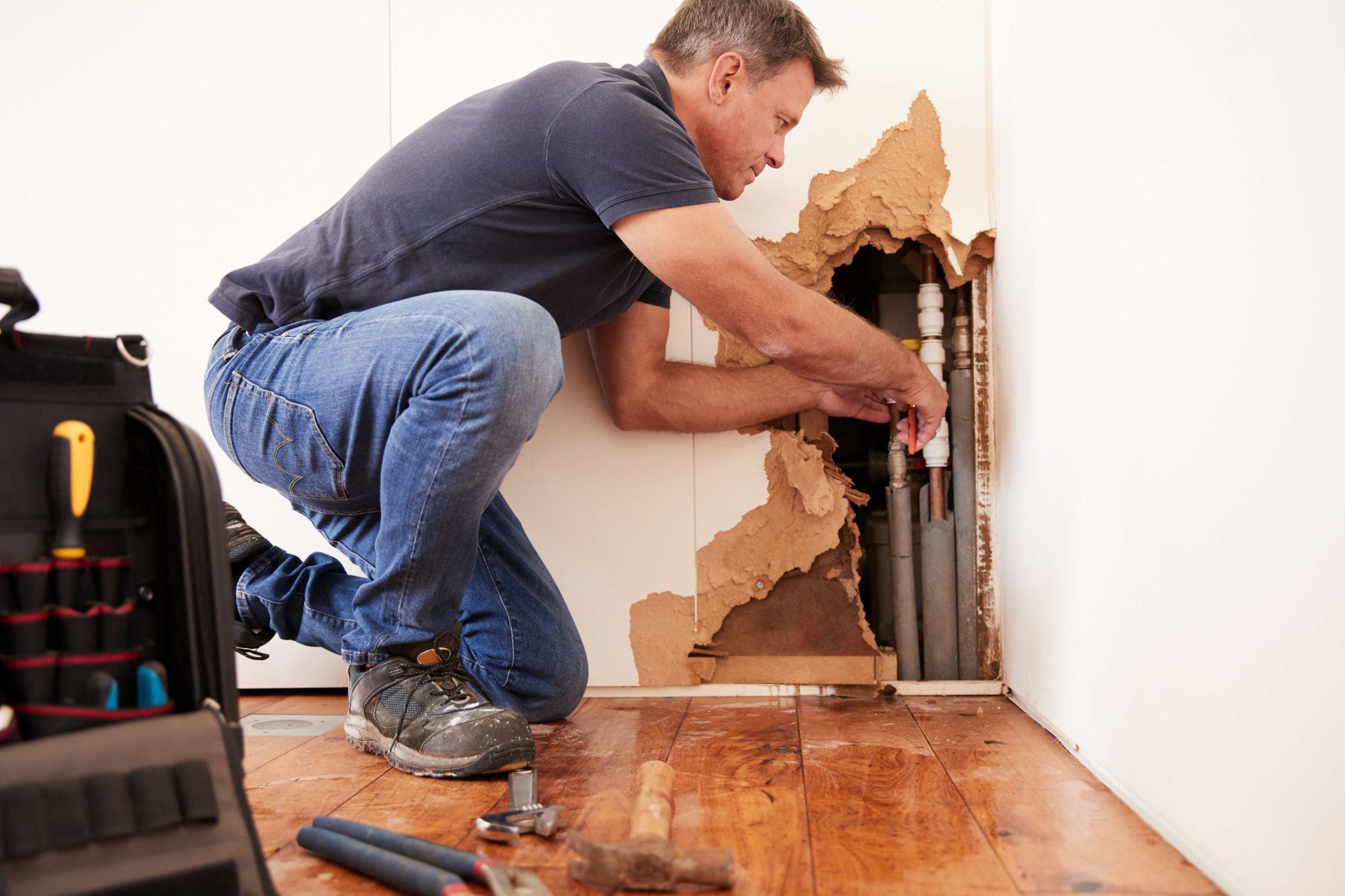a man is kneeling down in a room fixing a pipe .