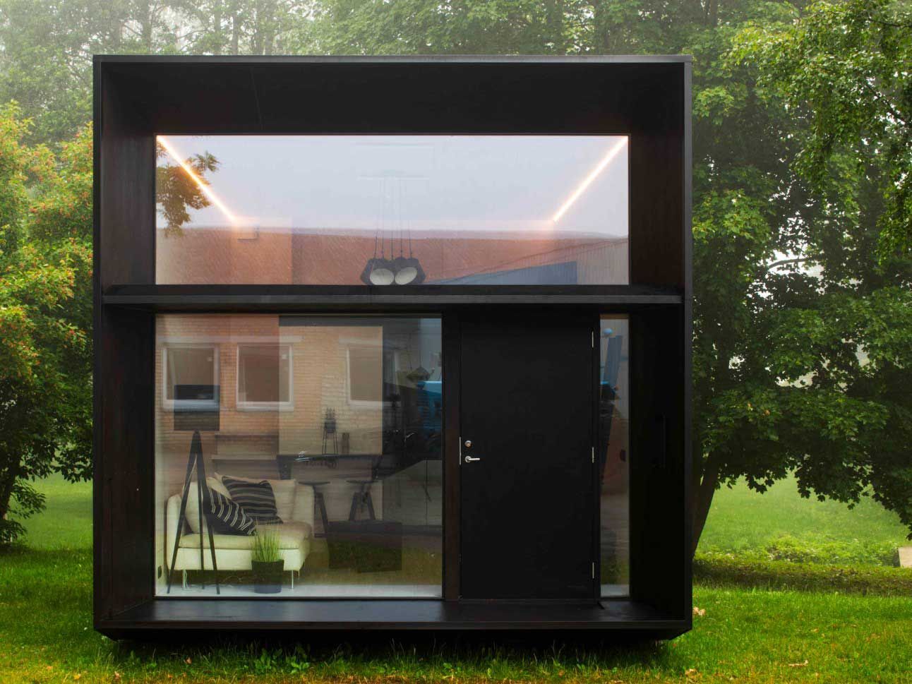 Modern, black box-shaped tiny house with large windows and door, set on grass.