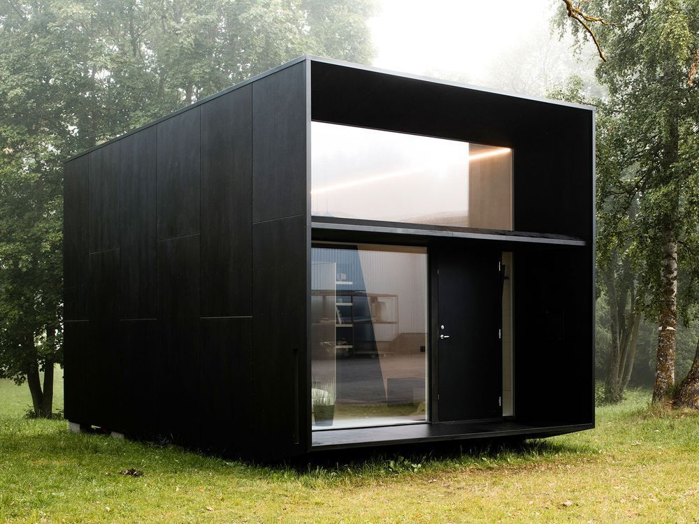 Black modern cabin with glass windows in a grassy forest.