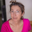 Woman with glasses and graying hair in a pink shirt, looking directly at the viewer.