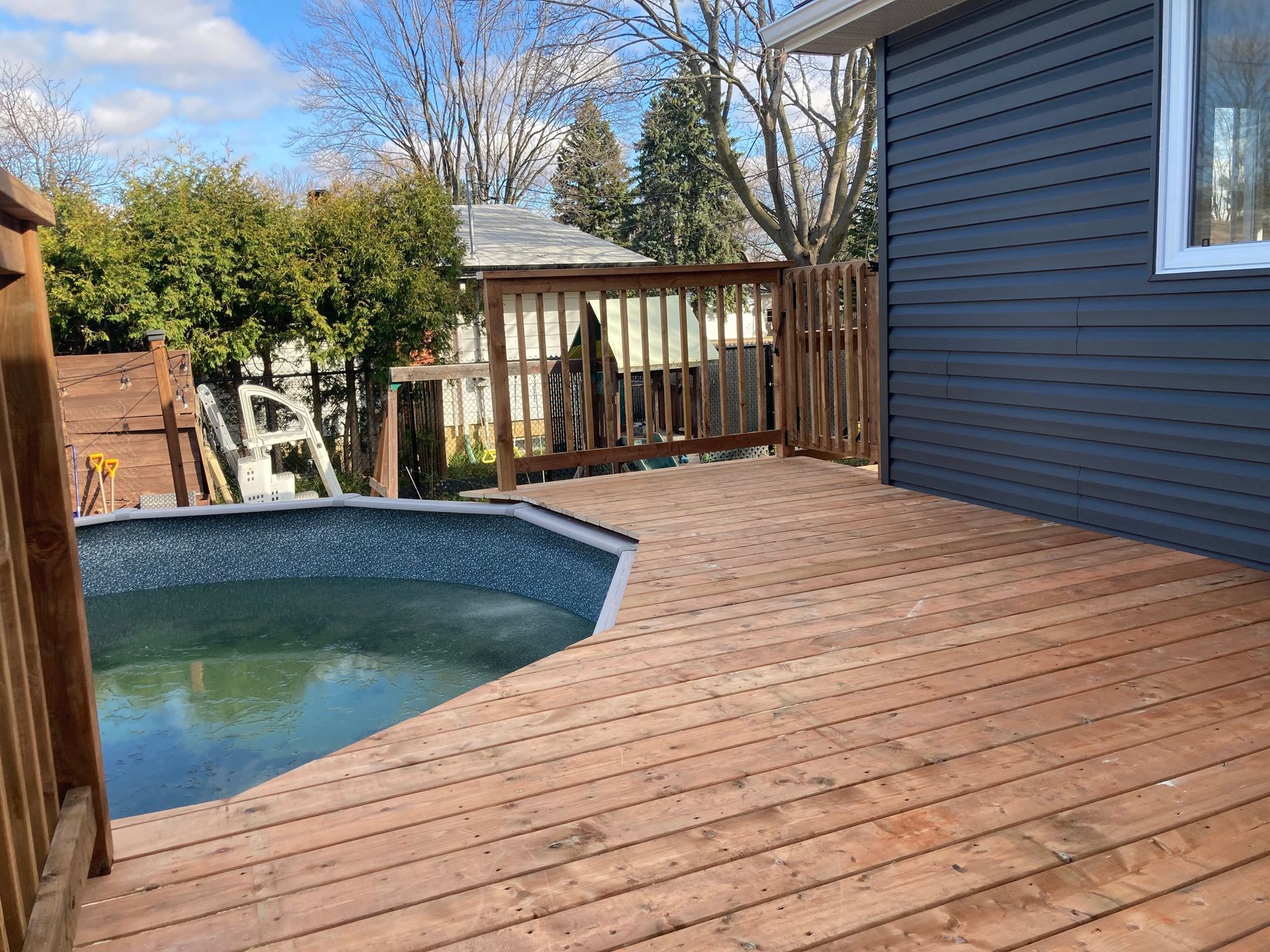 Une terrasse en bois avec une piscine en arrière-plan.