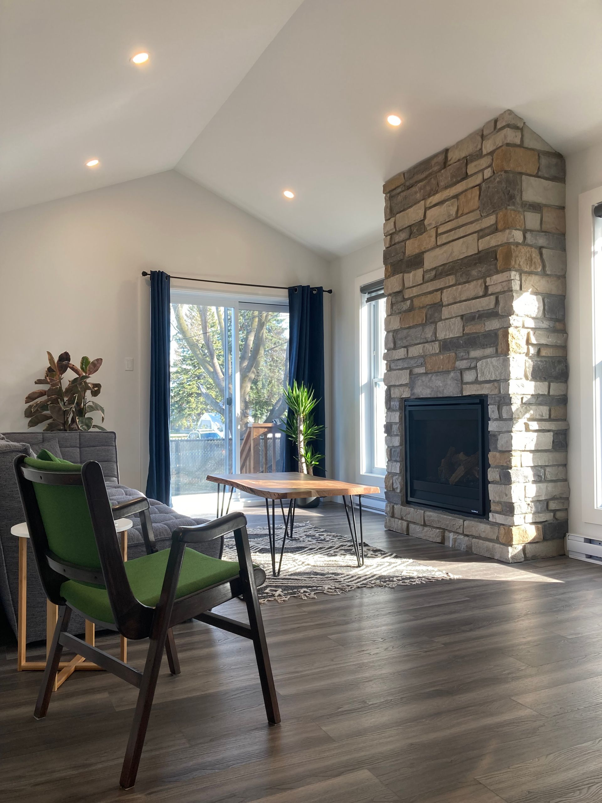 Un salon avec une cheminée en pierre et une chaise verte.