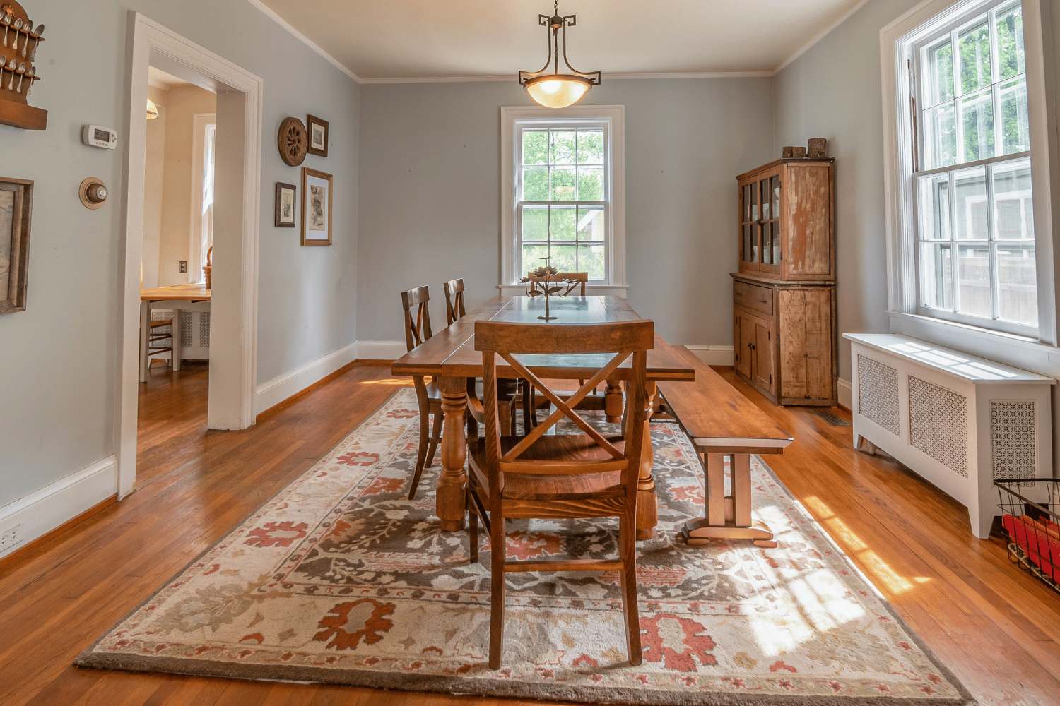 Dining room with light gray walls, a wooden table and chairs on a patterned rug, a hutch, and a doorway to another room.