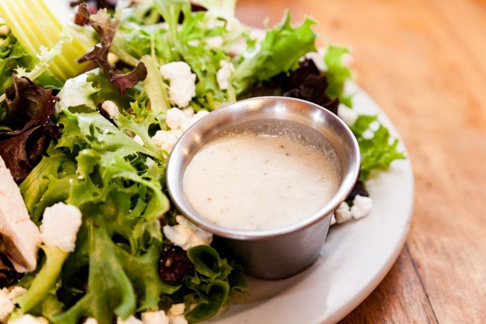 A salad with a small bowl of dressing on a plate.