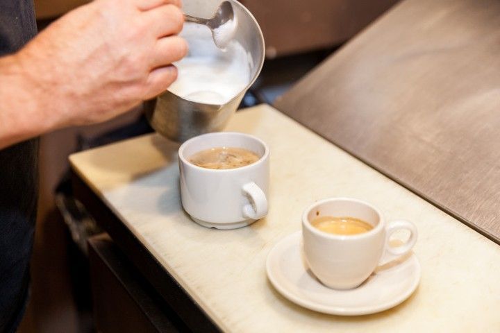 A person is pouring milk into two cups of coffee.