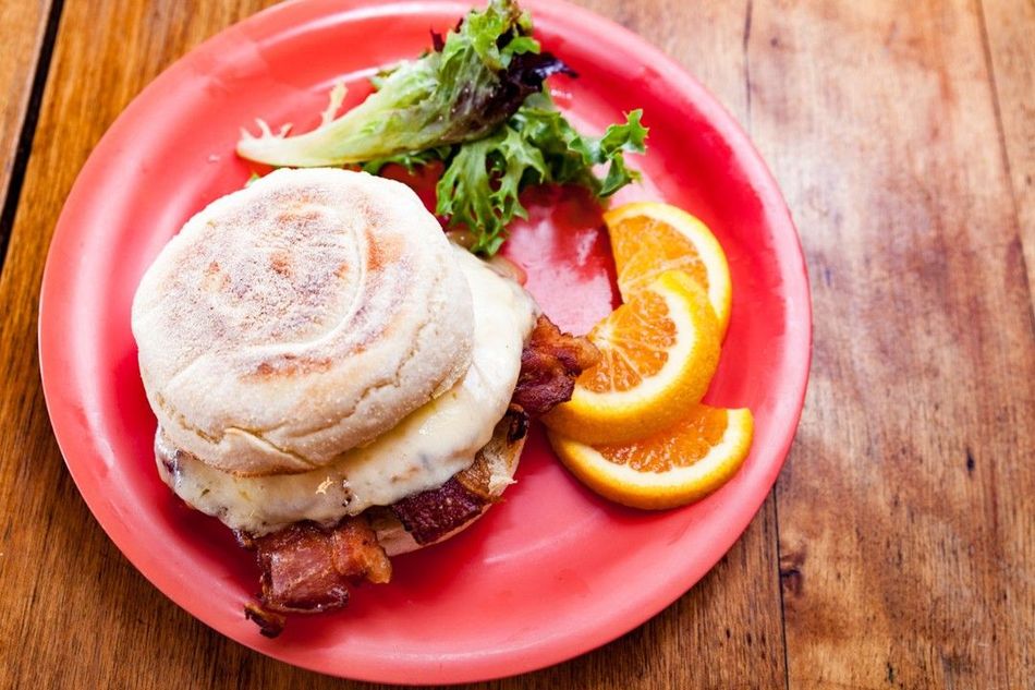 A red plate topped with a sandwich and oranges on a wooden table.