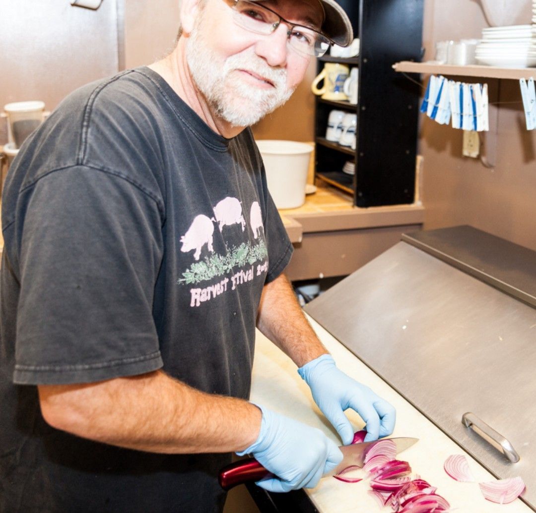 A man wearing a farmer 's market shirt is cutting onions