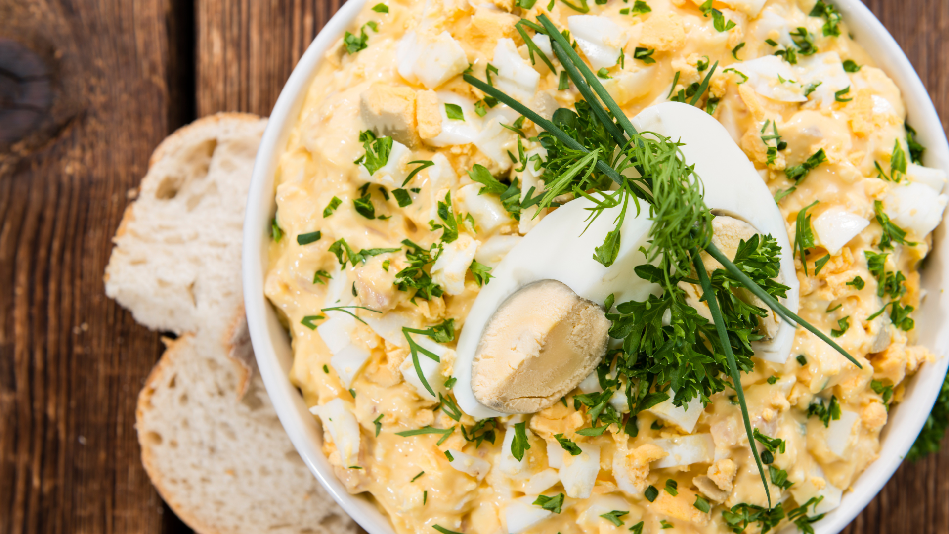 A bowl of scrambled eggs with sour cream and chives on a wooden table.