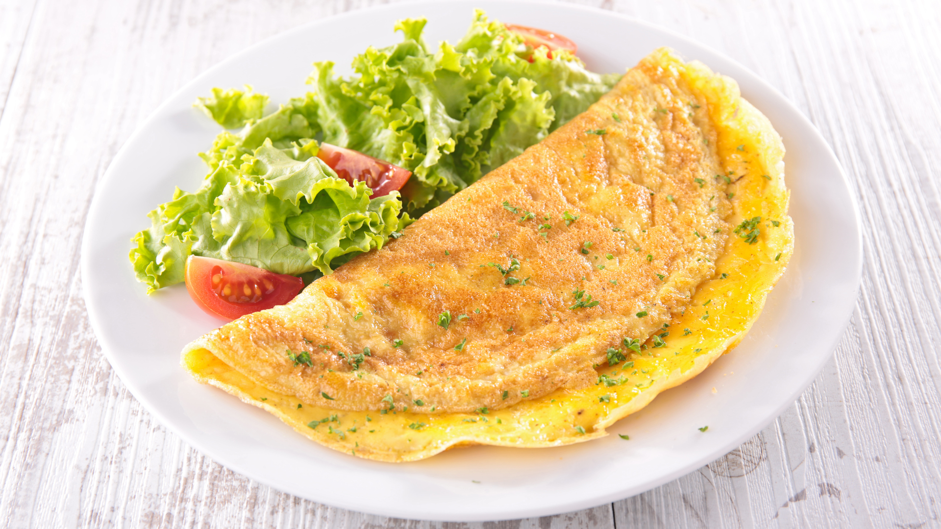 A white plate topped with an omelet and a salad.