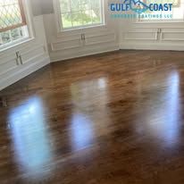 Shiny brown wood floor reflecting sunlight in a room with white trim and windows.