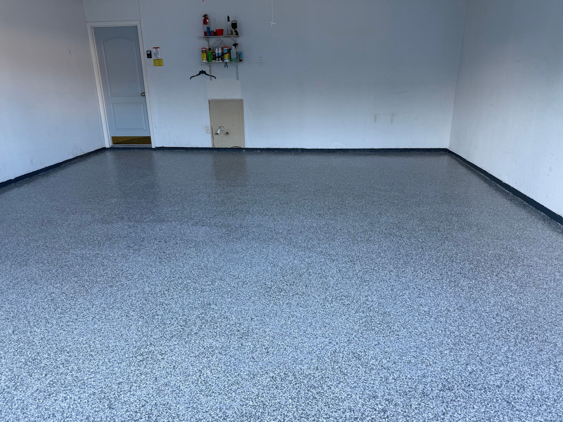 Garage interior with a gray speckled epoxy floor, white walls, and a door.
