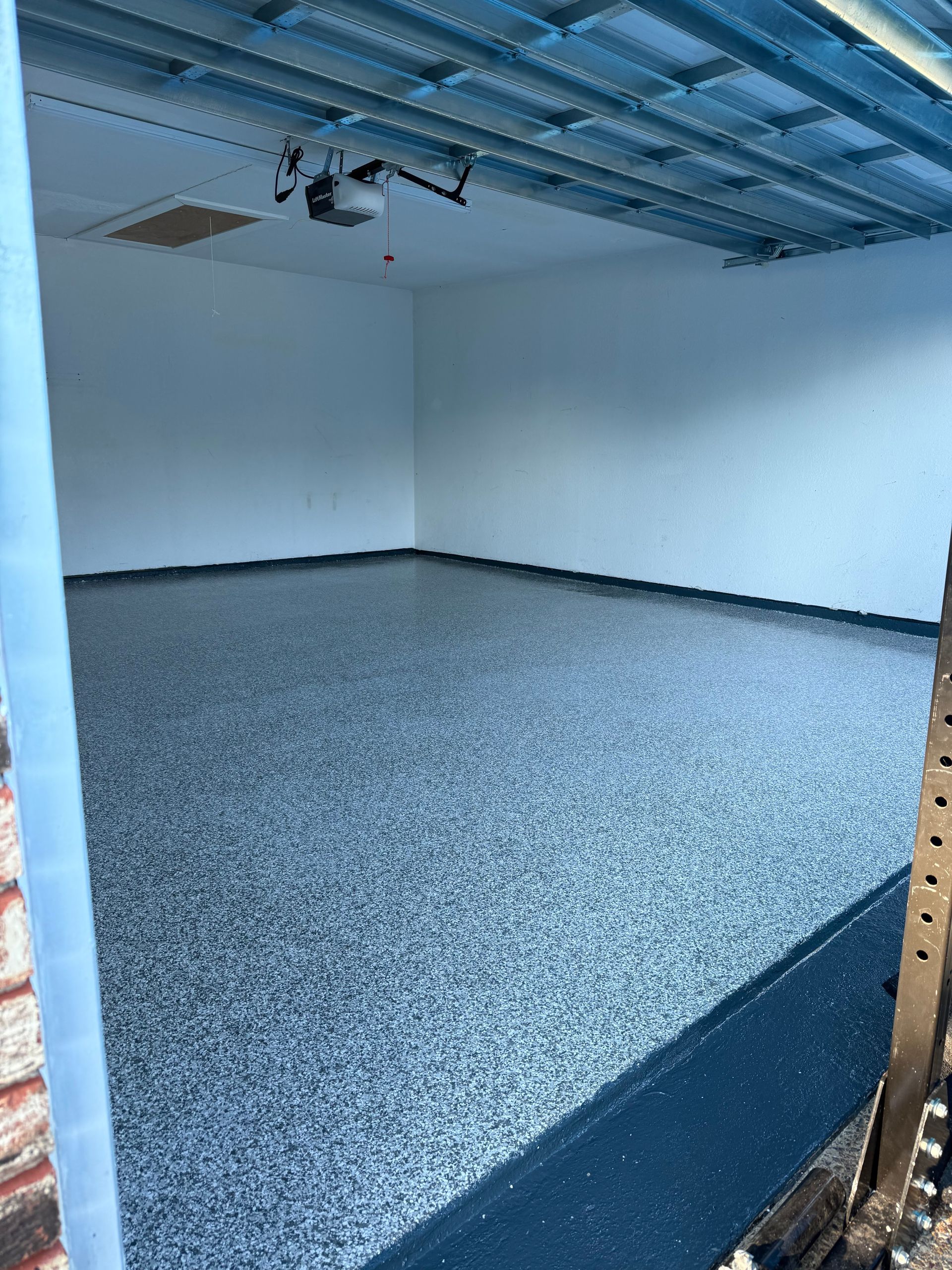 Garage interior with gray speckled floor, white walls, and exposed ceiling beams.