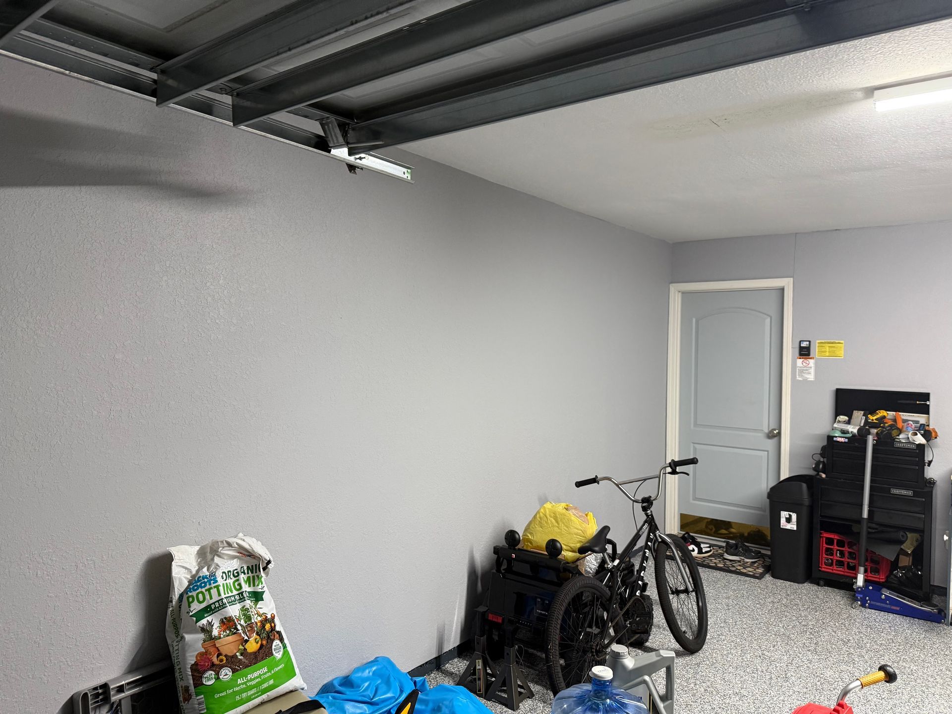 Gray garage interior with supplies, a bicycle, and a closed door.