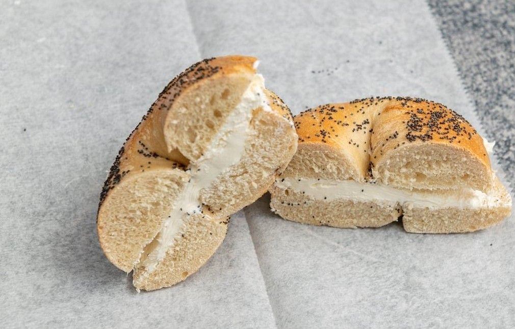 A bagel with cream cheese and poppy seeds is cut in half.