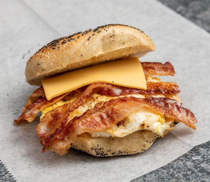 A bagel sandwich with eggs , bacon and cheese on a table.