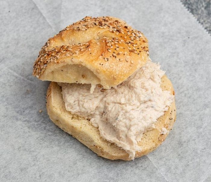 A bagel with tuna on it is cut in half on a piece of wax paper.