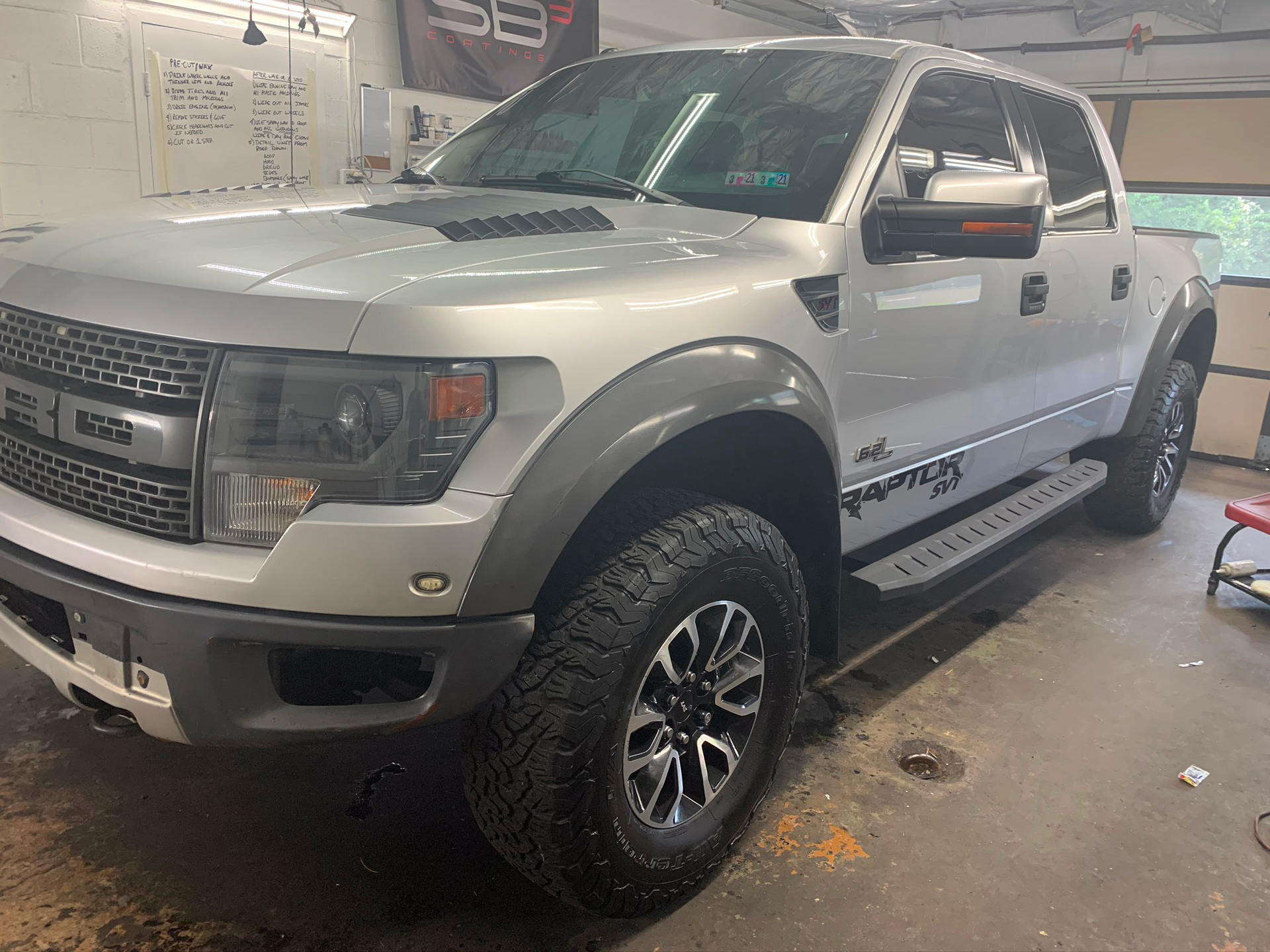 A silver ford raptor is parked in a garage.
