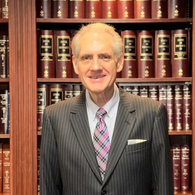 A man in a suit and tie is standing in front of framed diplomas