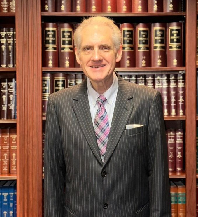 A man in a suit and tie is standing in front of a bookshelf filled with books.