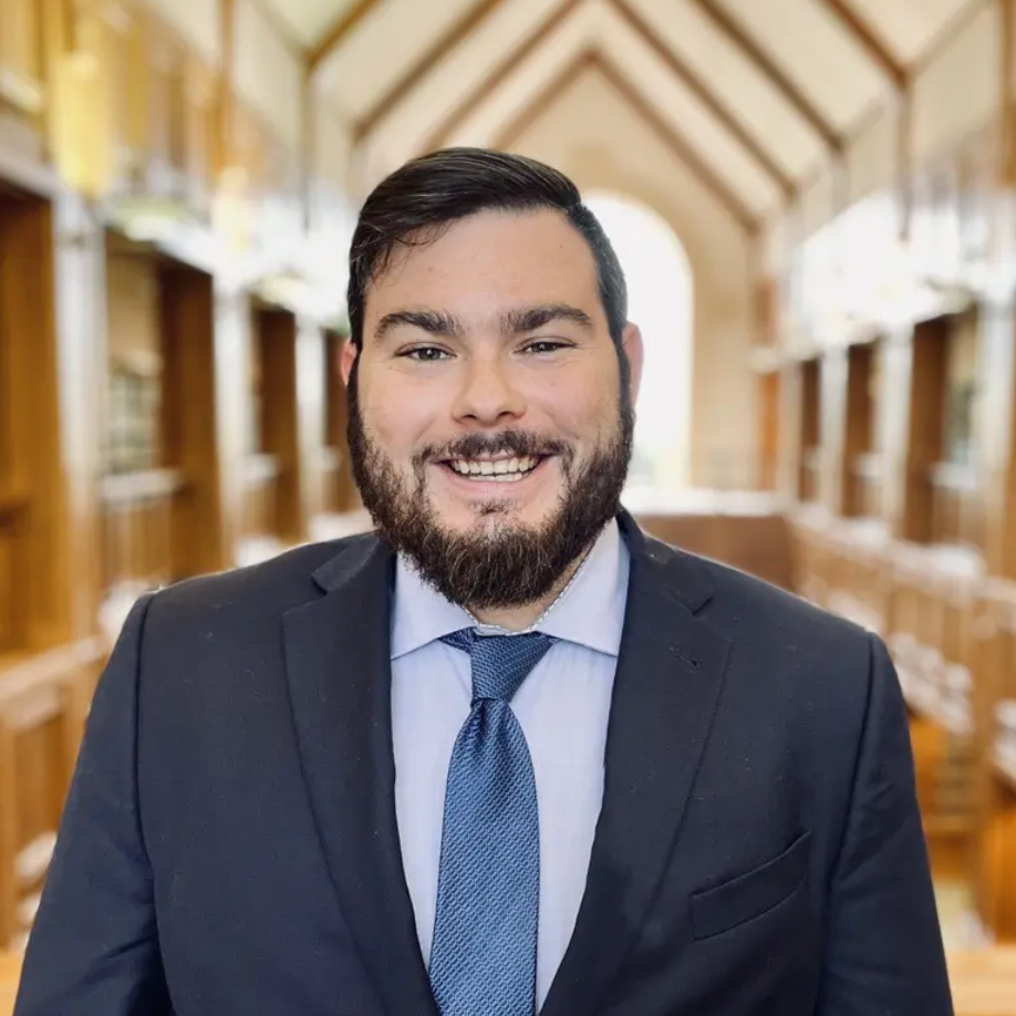 A man with a beard is wearing a suit and tie and smiling.