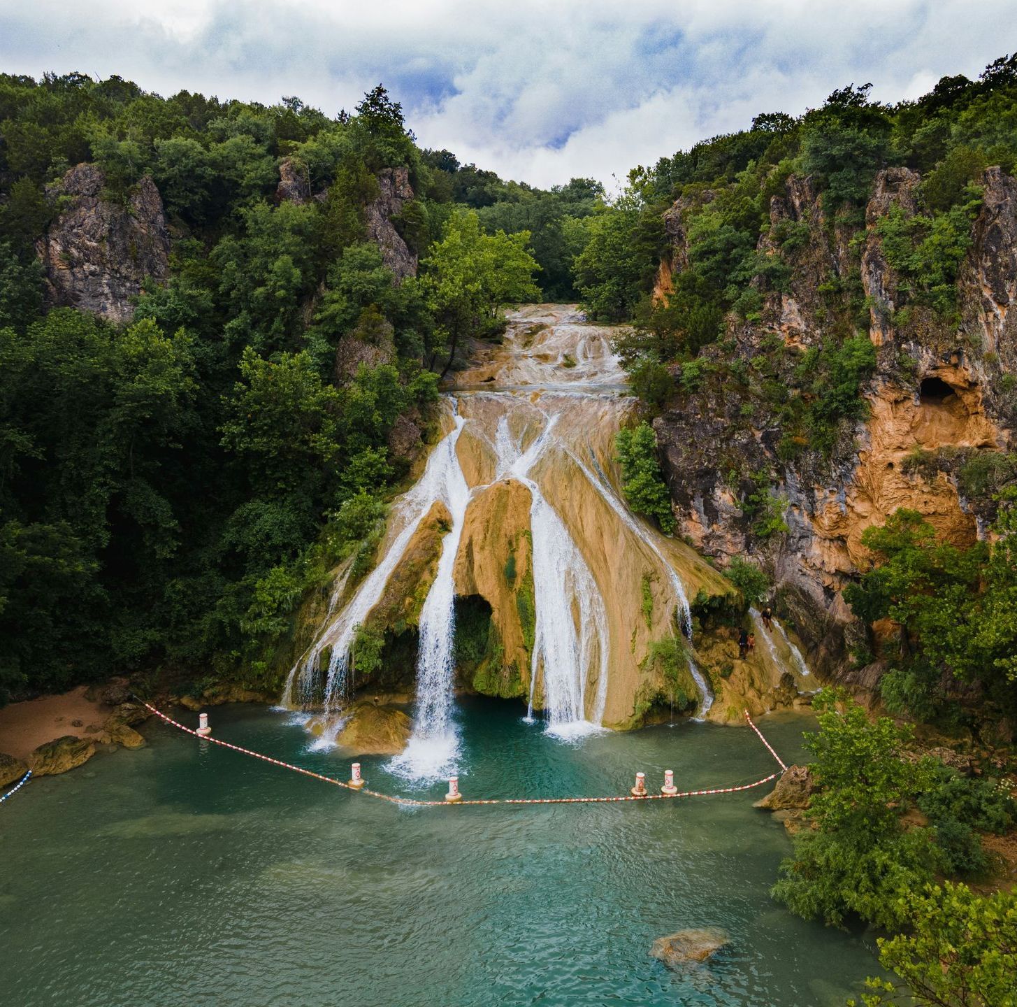 A waterfall is surrounded by trees and a body of water