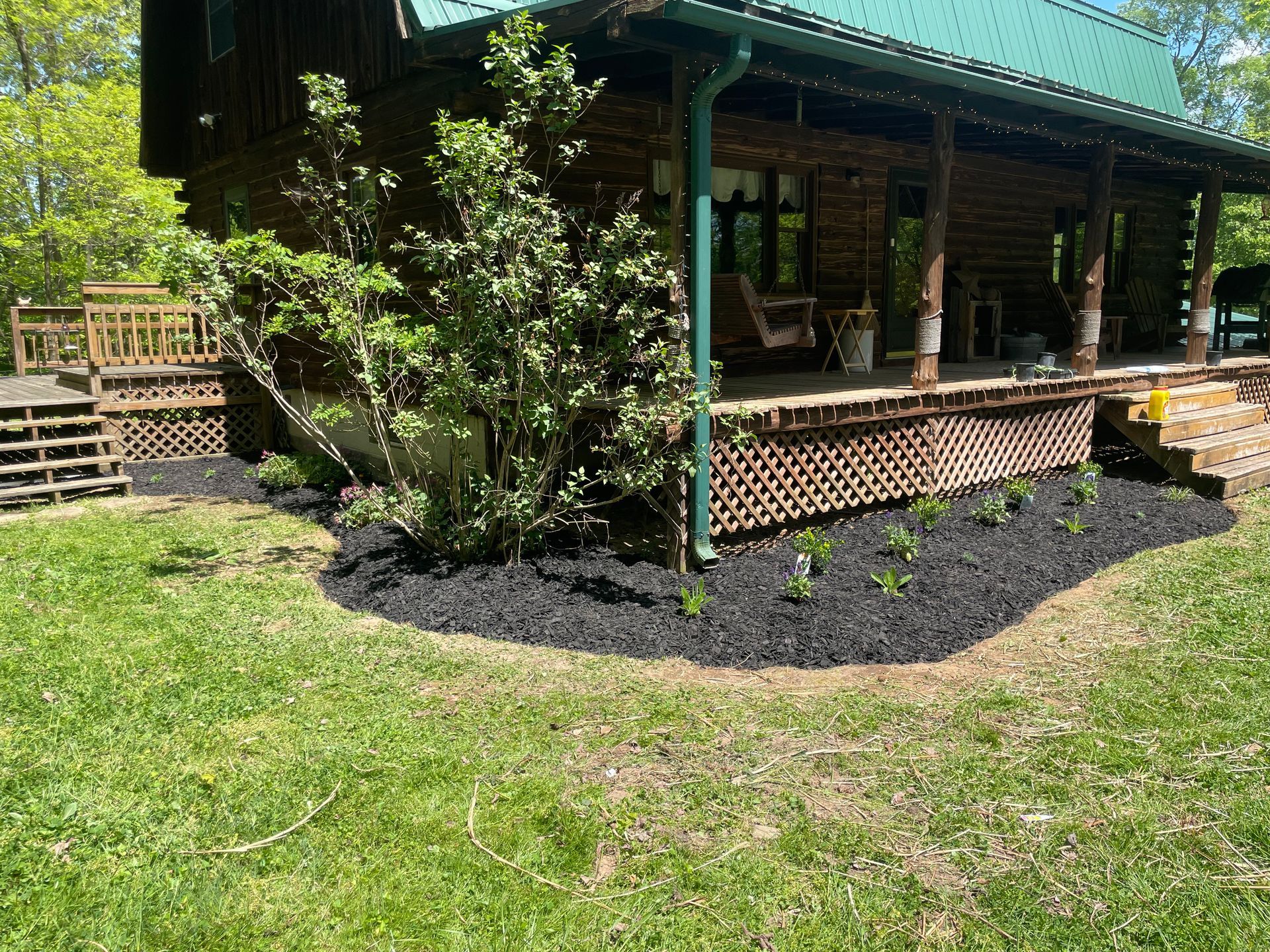 Green lawn and landscaped shrubs in front of a rustic porch with lattice skirting and green posts
