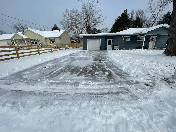 Snow-cleared driveway leading to a gray house and garage in a snowy residential neighborhood