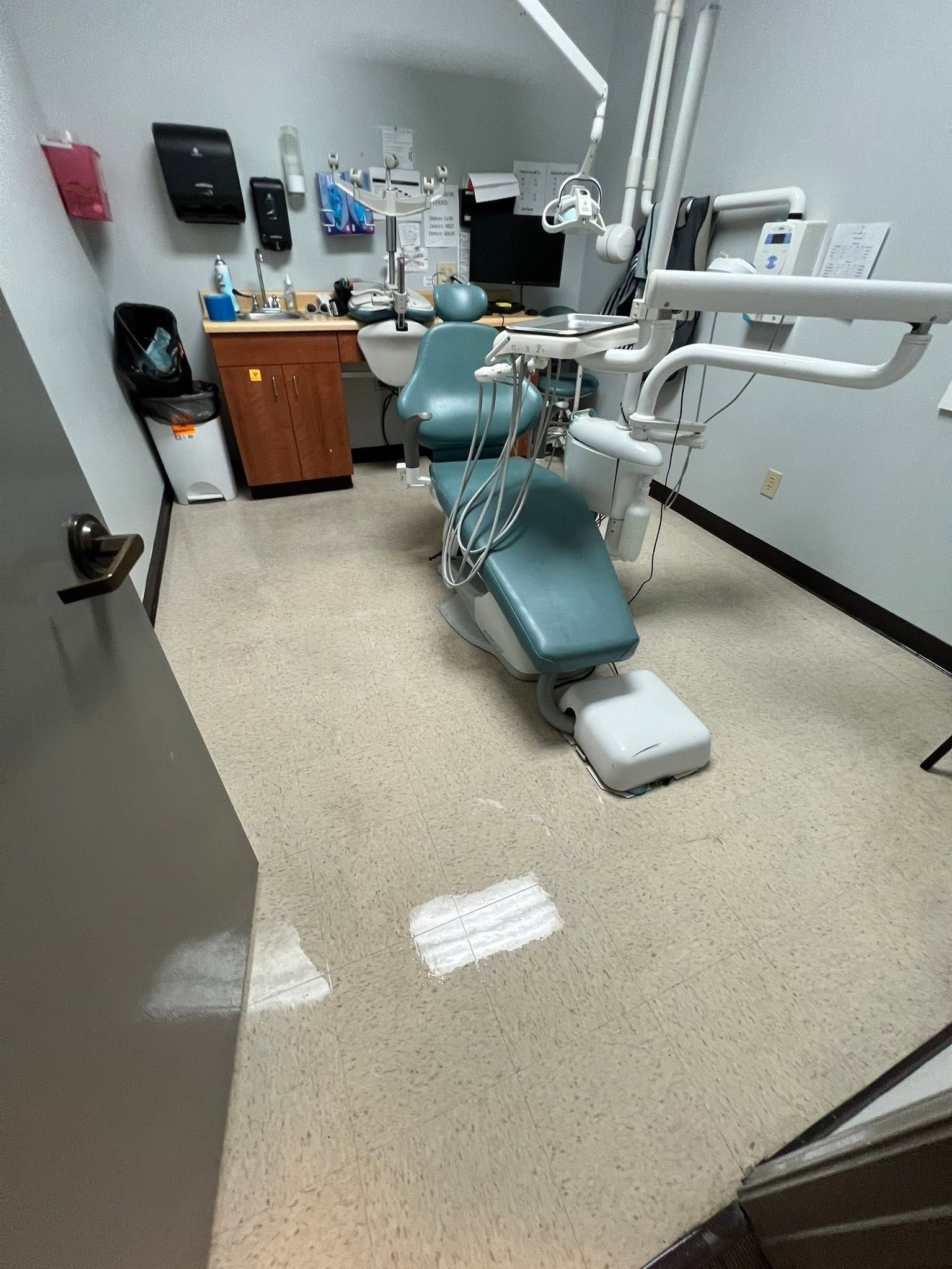 Dental exam room with teal chair, sink, cabinets, and medical equipment