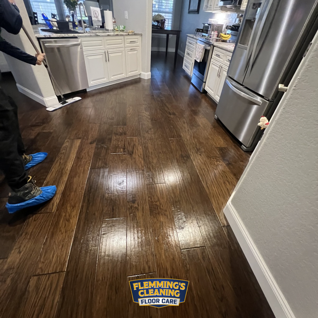 Kitchen with shiny dark hardwood floors, a person standing at left, and a cleaning service sticker on the floor.