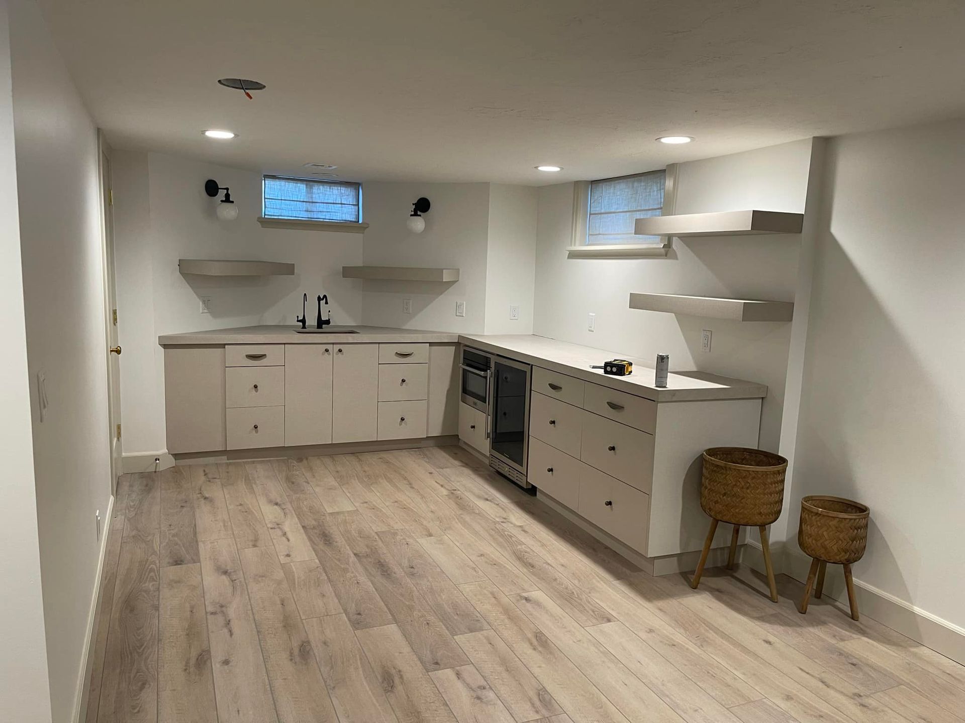 A kitchen with white cabinets and wooden floors in a basement.