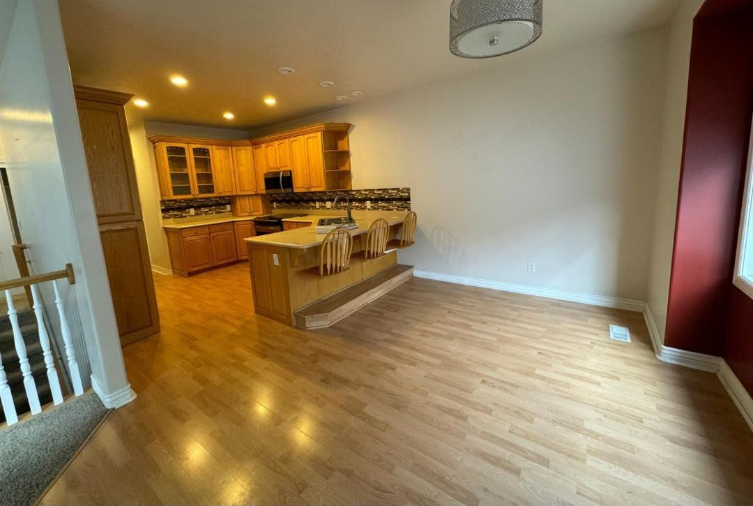 A living room with hardwood floors and a kitchen in the background.