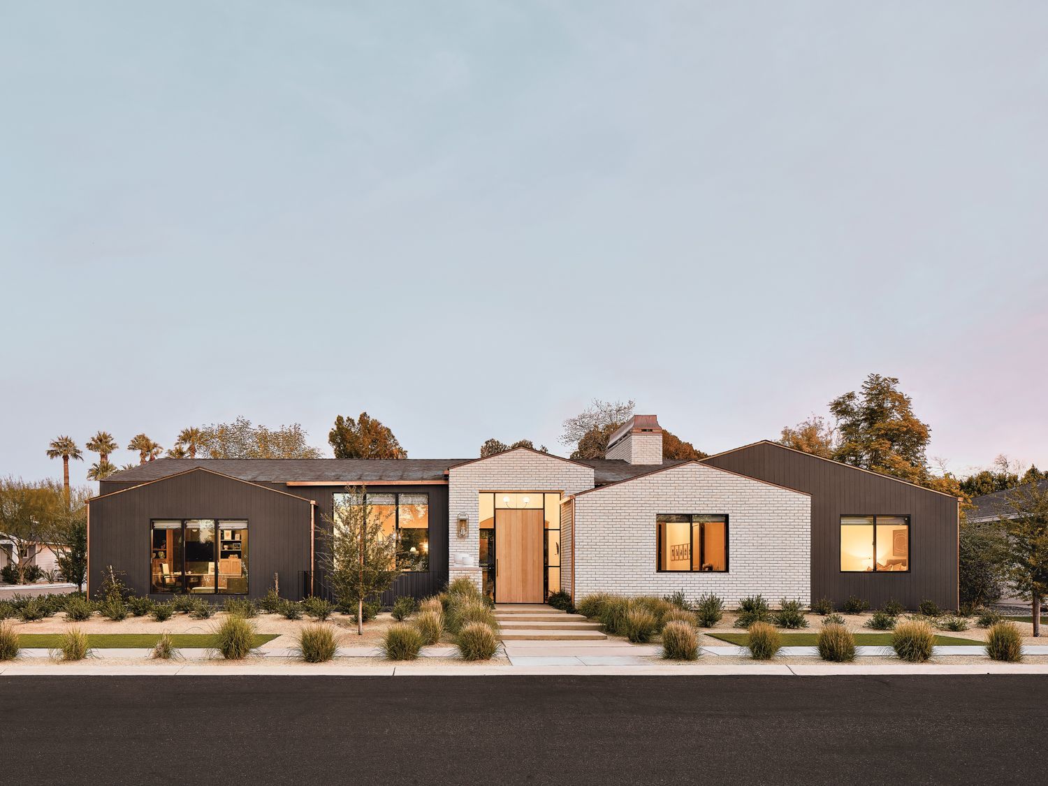 Modern home with black and white exterior, landscaping, and open front door.