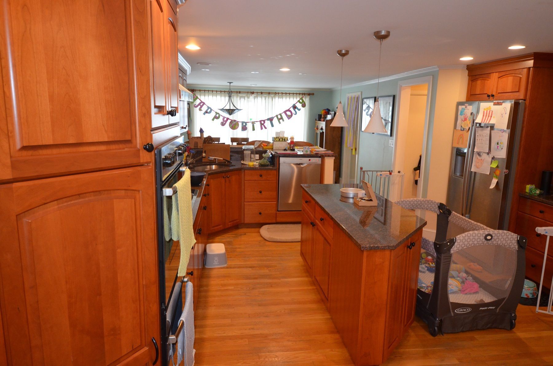 A kitchen with wooden cabinets , granite counter tops , stainless steel appliances and a baby crib.