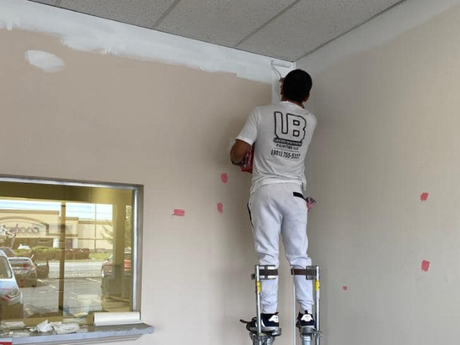 A man standing on stilts painting a wall with the letter b on his back