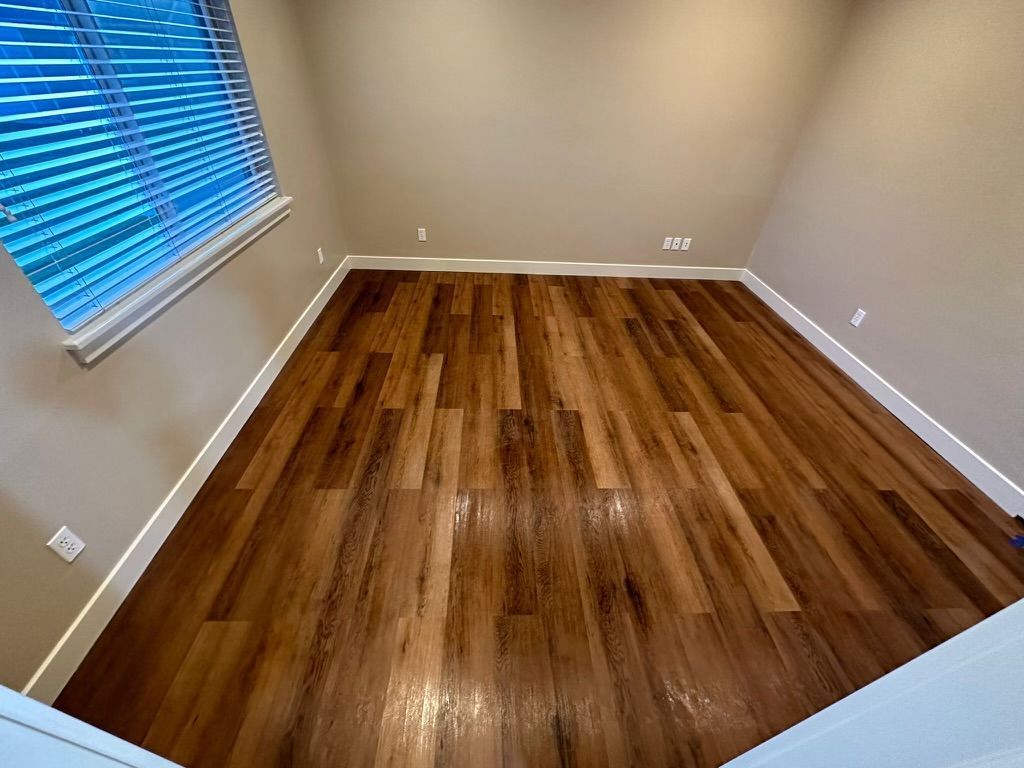 An empty room with hardwood floors and a window with blinds.